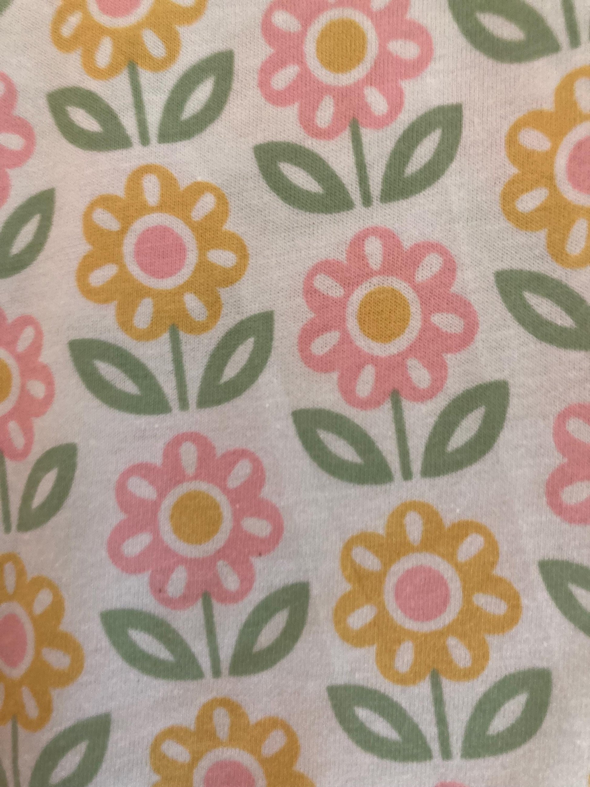 May include: Close-up of a white fabric with a repeating floral pattern. The flowers alternate between pink and yellow, each with a pink center. Green leaves and stems complete the design. The overall aesthetic is cheerful and reminiscent of spring.